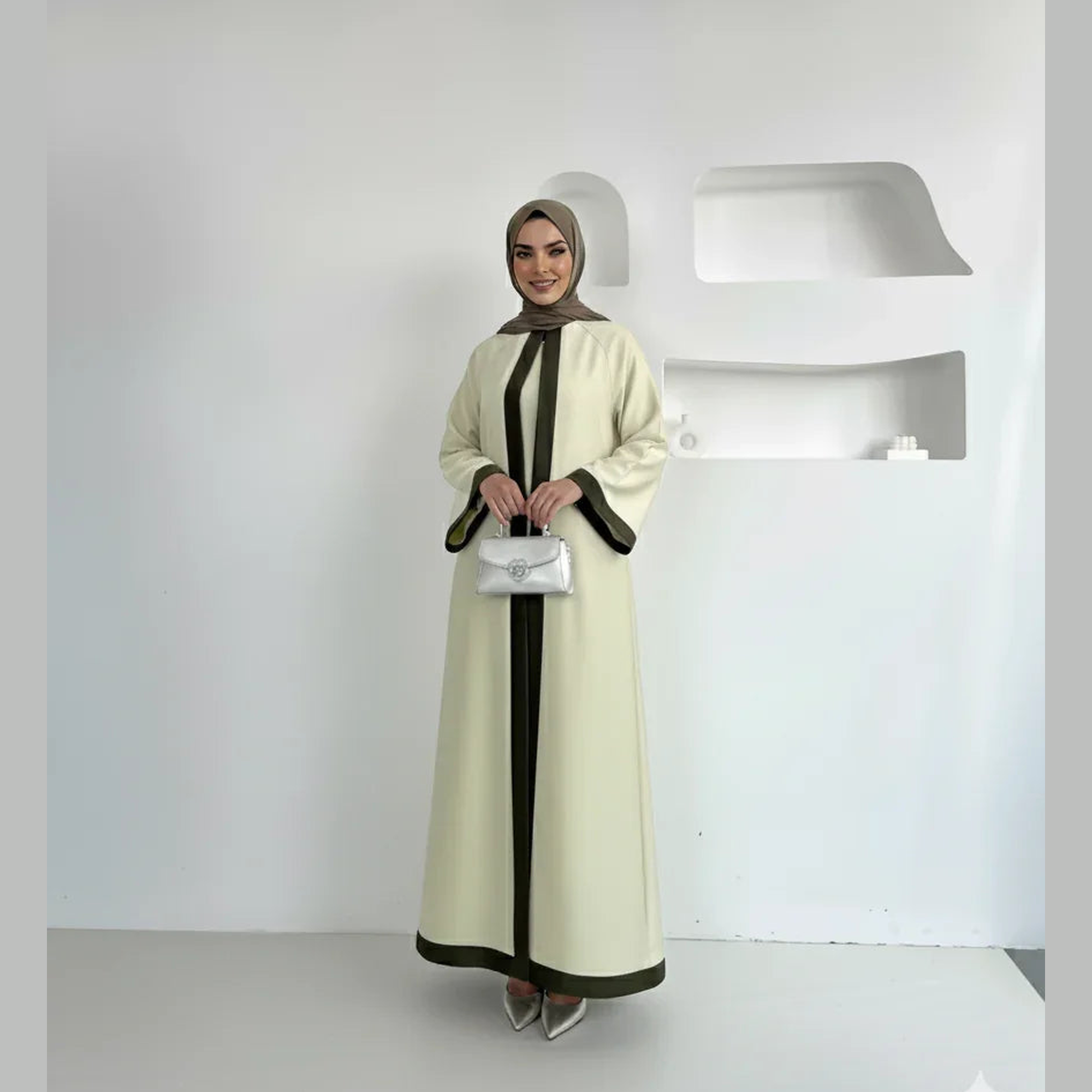 Elegant woman in modest cream abaya with dark trim, taupe hijab, and silver handbag, ZAHRA'S BEST fashion