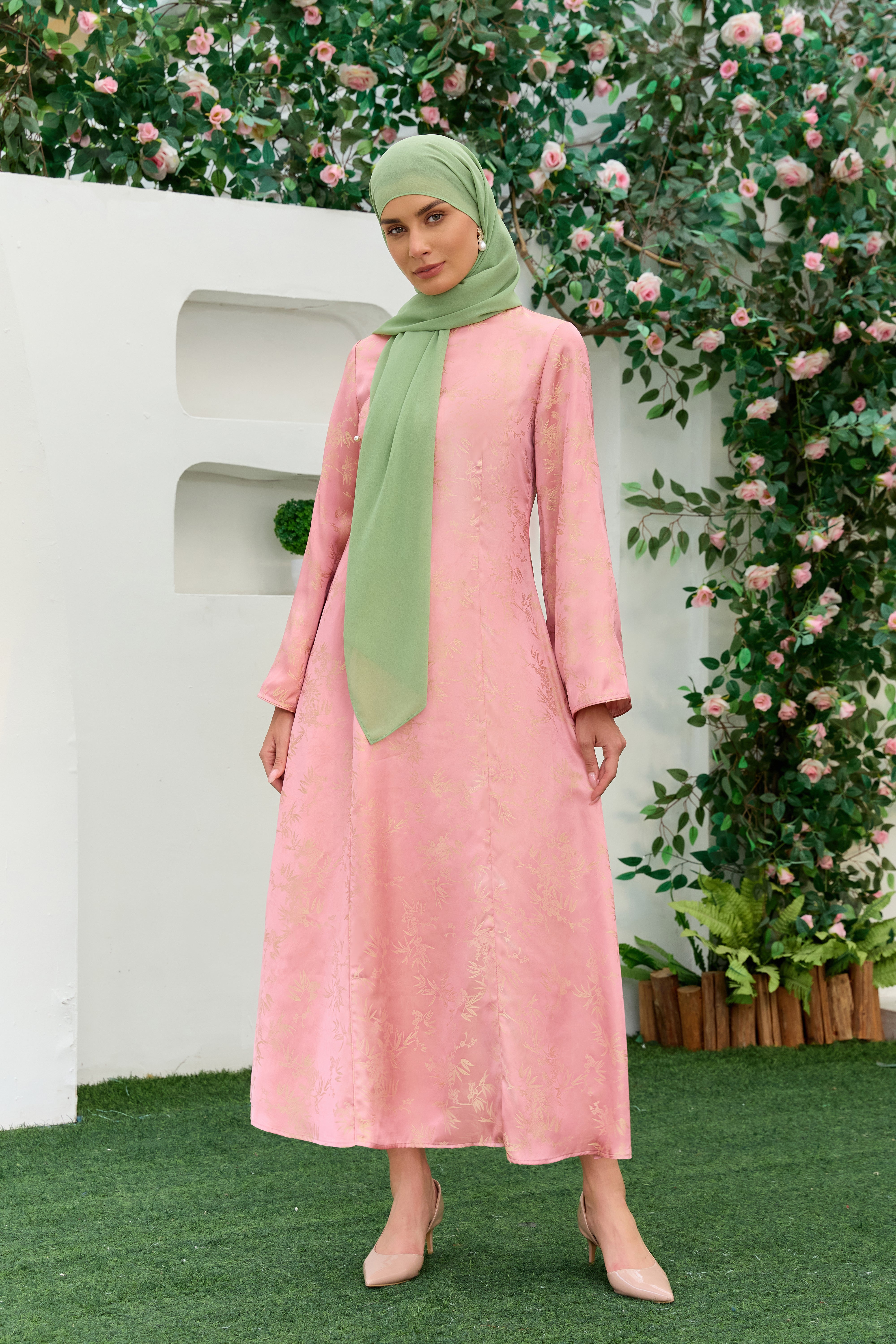 A woman wearing a long-sleeved pink jacquard Cheongsam inspired and a sage green hijab- Zahras Best