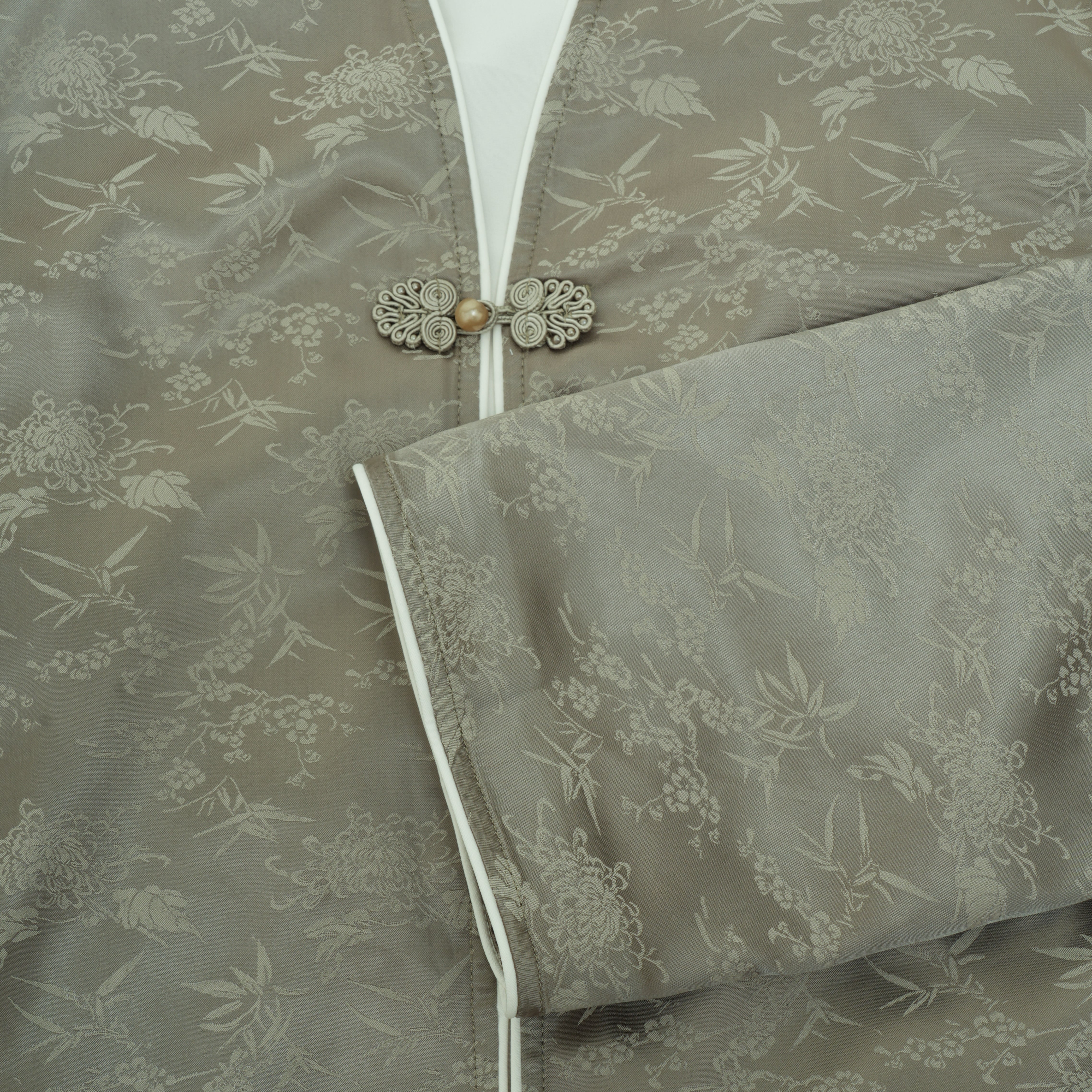 Close-up of a taupe brocade jacket with a floral bamboo pattern, featuring a silver-tone metal button closure and a matching folded cuff.