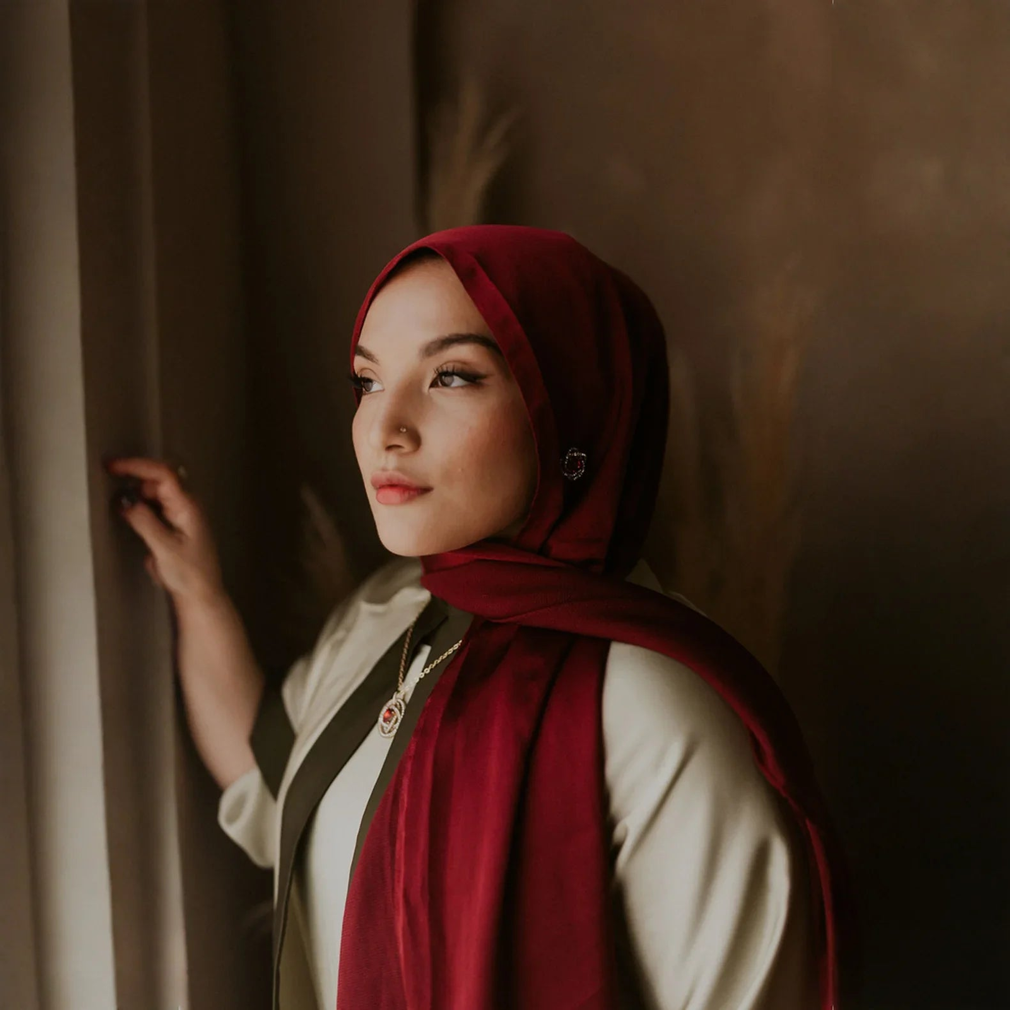 Woman in elegant maroon hijab and cream modest wear by window, ZAHRA'S BEST fashion